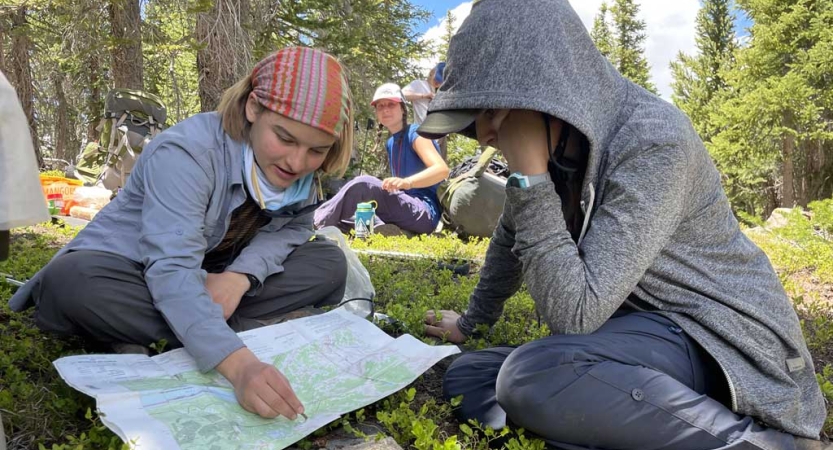 two students examine a map while sitting on green grass